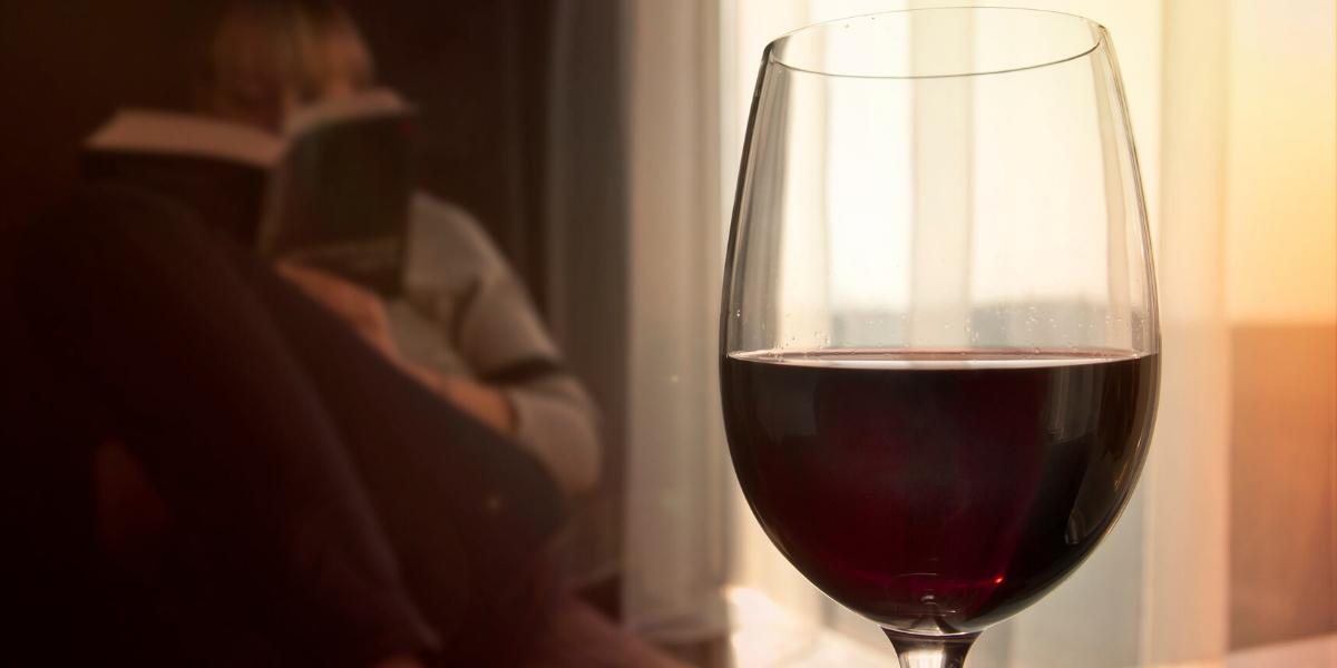 A woman reading one of the best beginner wine books with a glass of red wine in the foreground